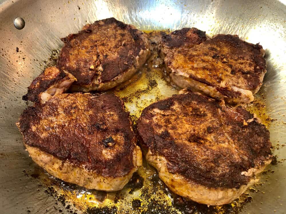 Filet mignon frying in a pan