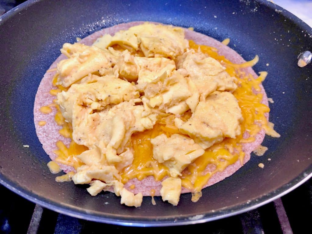 Eggs added to cheesy tortilla in a pan