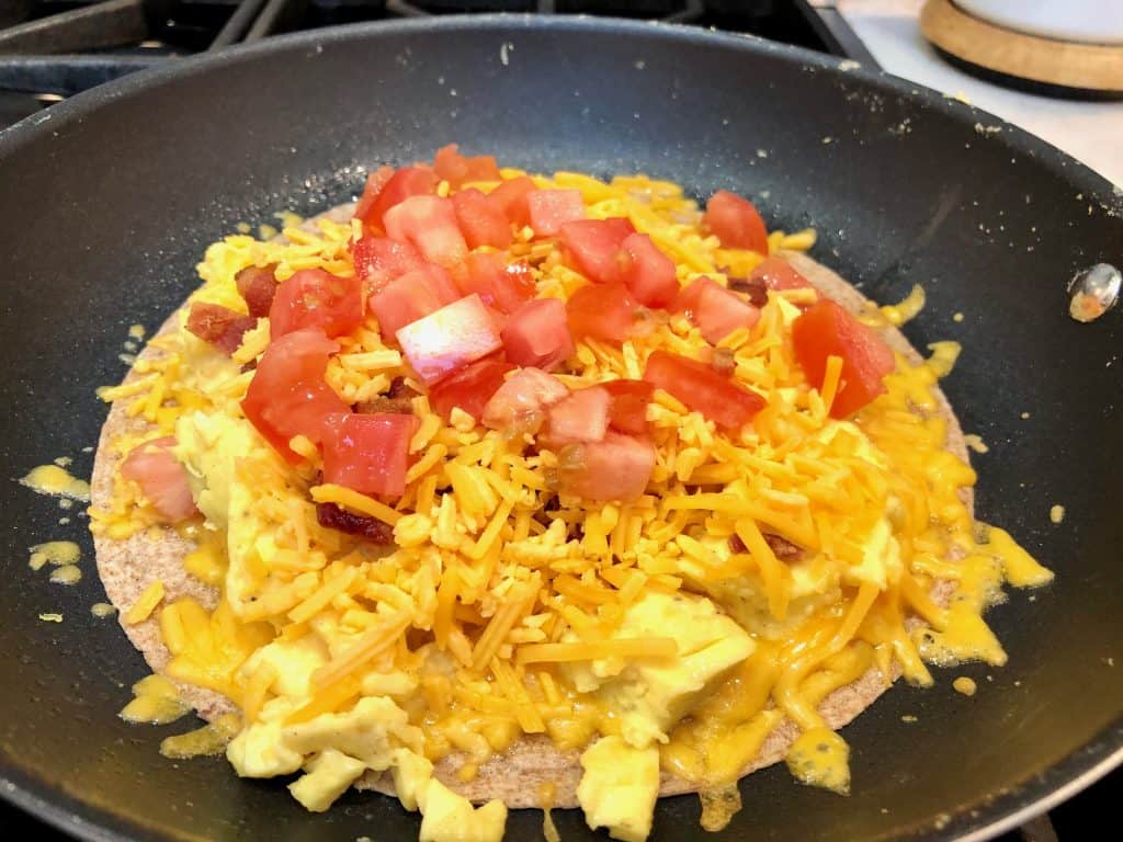 Cheesy egg tortilla with bacon and tomato in a pan