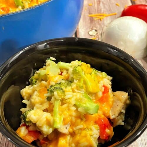 a closeup picture of a cheesy chicken and rice with vegetables recipe in a bowl.